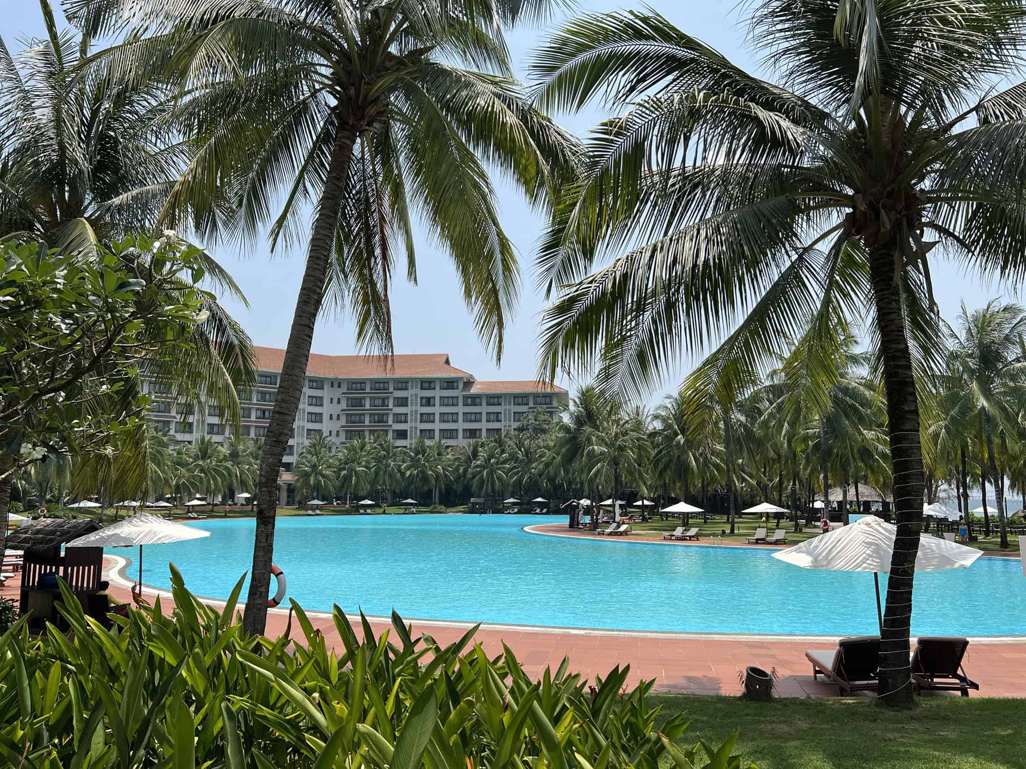 A view through palm trees of the huge swimming pool at the VinPearl Resort and Spa Phu Quoc